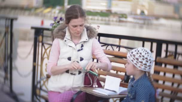 Kleine, mooi, lgirl en haar moeder zit op bankje in park, in handen van haar notitieblok. Ze is het dragen van een jas. Zij maakt van notities en ziet er zeer romantisch. — Stockvideo