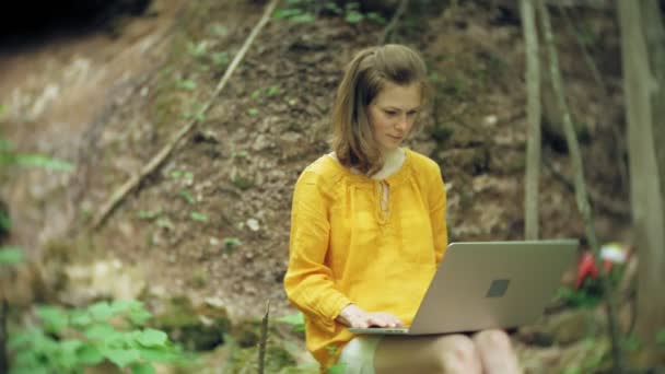 Mädchen mit Laptop sitzt auf einem Felsen im Wald — Stockvideo