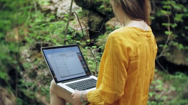 Dívka s notebookem, sedící na skále, v lese — Stock video