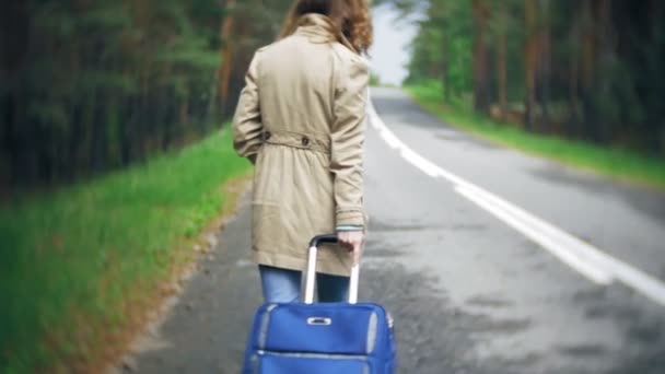 Νεαρή όμορφη γυναίκα ωτοστόπ στέκεται στο δρόμο με μια βαλίτσα σε ένα τραπέζι με μια επιγραφή στη θάλασσα — Αρχείο Βίντεο