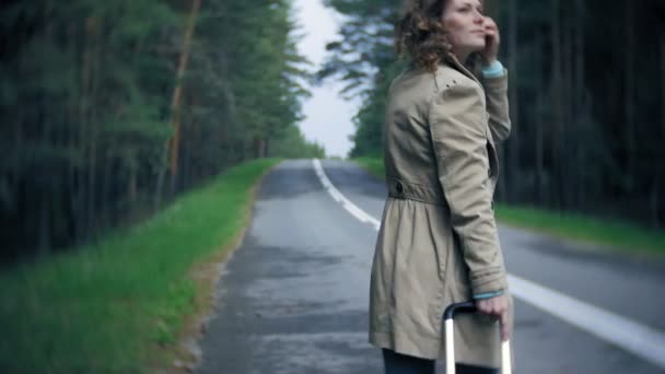 海の碑文を持つテーブルでスーツケースを道路上に若い美しい女性ヒッチハイク立って — ストック動画