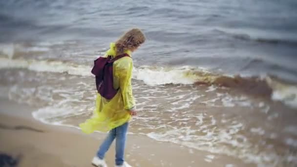 Sahil boyunca seyahat yaşam tarzı macera tatil açık havada yürüyen mutlu kadın. Bir moda sarı yağmurluk giymiş bir kız — Stok video