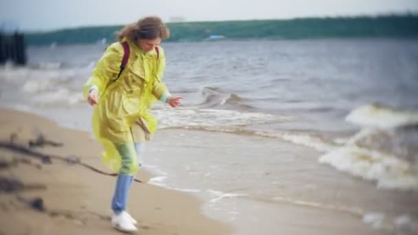 Mujer feliz caminando por la costa Viajando Estilo de vida aventura vacaciones al aire libre. Una chica vestida con un impermeable amarillo de moda — Vídeo de stock