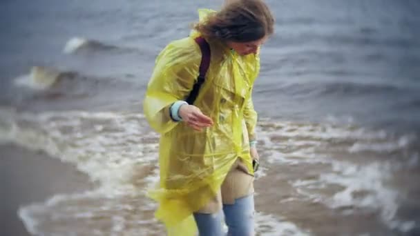 幸せな女のライフ スタイルの旅冒険休暇屋外の海岸に沿って歩きます ファッショナブルな黄色のレインコートを着た女の子 — ストック動画