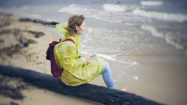 Lycklig kvinna promenader längs kusten reser livsstil äventyr semester utomhus. En flicka klädd i en fashionabel gul regnrock — Stockvideo