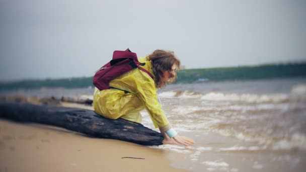 Ευτυχισμένη γυναίκα το περπάτημα κατά μήκος της ακτής του τρόπου ζωής που ταξιδεύουν περιπέτεια διακοπές σε εξωτερικούς χώρους. Ένα κορίτσι που είναι ντυμένος με ένα μοντέρνο κίτρινο αδιάβροχο — Αρχείο Βίντεο