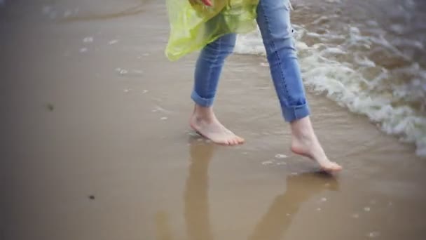 Mulher feliz andando ao longo da costa Viajando Lifestyle aventura férias ao ar livre. Uma menina vestida com uma capa de chuva amarela elegante — Vídeo de Stock