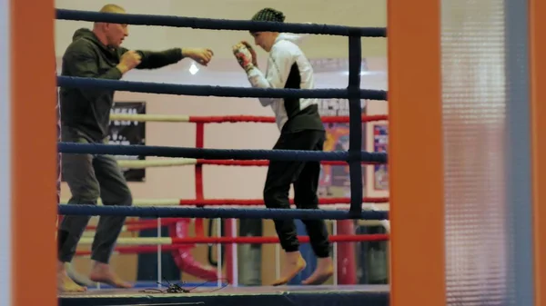 O treinador conduz uma batalha de treinamento com uma mulher kickboxer no ringue — Fotografia de Stock