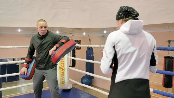 O treinador conduz uma batalha de treinamento com patas com uma mulher kickboxer no ringue — Fotografia de Stock