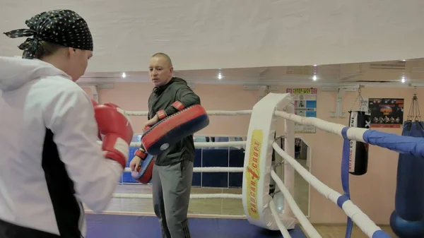 El entrenador lleva a cabo una batalla de entrenamiento con las patas con una kickboxer femenina en el ring —  Fotos de Stock