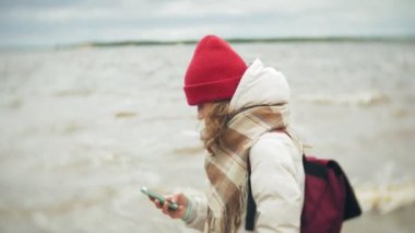 Kırmızı bir şapka müzik ve nehir kıyısında yürüme rahat genç kadın. Atış ayarı gerçek zamanlı izleme