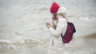 Kırmızı bir şapka müzik ve nehir kıyısında yürüme rahat genç kadın. Atış ayarı gerçek zamanlı izleme