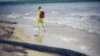 Sahil boyunca seyahat yaşam tarzı macera tatil açık havada yürüyen mutlu kadın. Bir moda sarı yağmurluk giymiş bir kız
