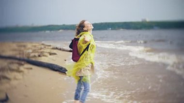 Sahil boyunca seyahat yaşam tarzı macera tatil açık havada yürüyen mutlu kadın. Bir moda sarı yağmurluk giymiş bir kız