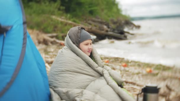 Tenda turística na margem do rio. a menina senta-se perto da tenda e olha para o rio . — Vídeo de Stock