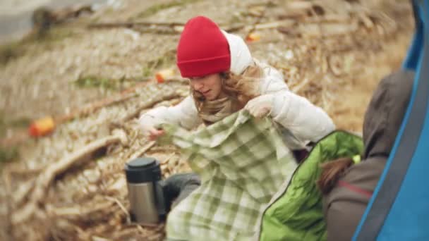 Turistický stan na břehu řeky. dvě dívka sedí u stanu, jídla a pití se dívá na řece. — Stock video