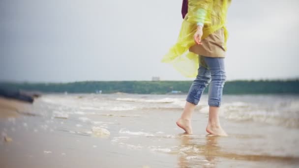 Gelukkige vrouw wandelen langs de kust Lifestyle reizen avontuurlijke vakantie buitenshuis. Een meisje gekleed in een modieuze gele regenjas — Stockvideo