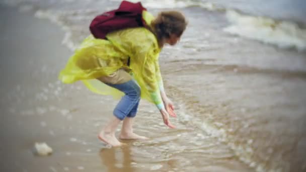 幸せな女のライフ スタイルの旅冒険休暇屋外の海岸に沿って歩きます。おしゃれな黄色のレインコートを着た女の子 — ストック動画