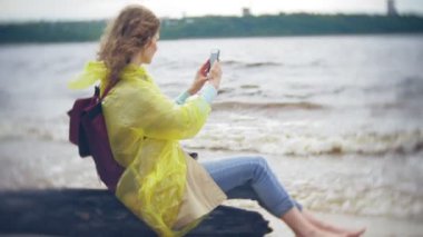 Sahil boyunca seyahat yaşam tarzı macera tatil açık havada yürüyen mutlu kadın. Bir moda sarı yağmurluk giymiş bir kız