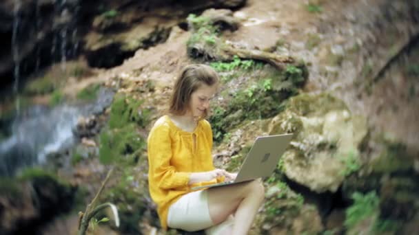 Mädchen mit Laptop sitzt auf einem Felsen im Wald — Stockvideo