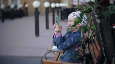 Bir telefon ile büyüleyici bir kız parkta elini kolunu sallaya dönüyor ve fotoğraf çeker