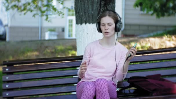 Joven mujer hermosa con estilo, en las calles de la ciudad escuchando música en los auriculares del monitor grande . — Vídeos de Stock