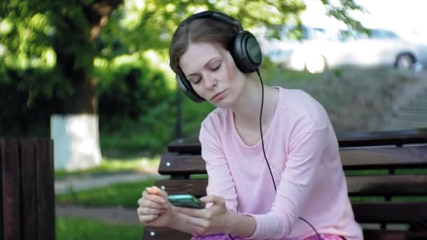 Joven mujer hermosa con estilo, en las calles de la ciudad escuchando música en los auriculares del monitor grande . — Vídeo de stock