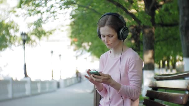 Mladé stylové krásná žena, na ulicích města poslechu hudby ve velkém monitoru sluchátka. — Stock video