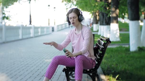 Junge, stylische, schöne Frau, die auf den Straßen der Stadt Musik mit Kopfhörern am großen Monitor hört. — Stockvideo