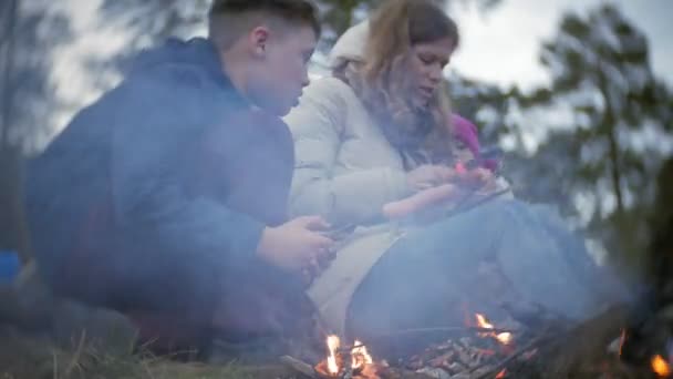 Šťastná rodina turistů na cestě. Máma a děti osmahneme klobásy do ohně u stanu — Stock video