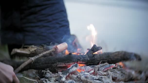 Família feliz de turistas em uma viagem. Mãe e crianças fritam salsichas no fogo perto da tenda — Vídeo de Stock