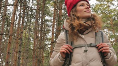 Çekici bir genç kadın kırmızı şapkalı bir büyük turistik sırt çantası ile erken baharda ormanda yürür