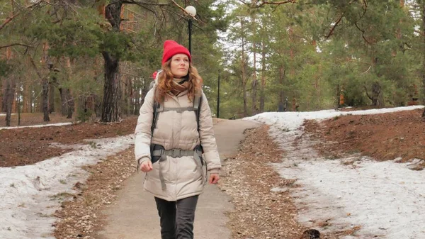 Une jolie jeune femme au chapeau rouge se promène dans la forêt au début du printemps avec un grand sac à dos touristique — Photo