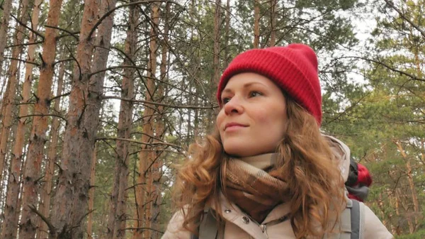 Çekici bir genç kadın kırmızı şapkalı bir büyük turistik sırt çantası ile erken baharda ormanda yürür — Stok fotoğraf