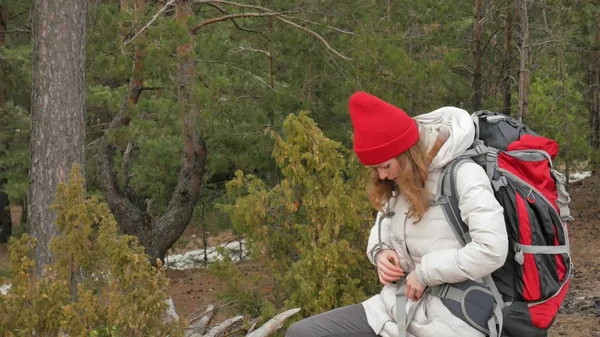 Eine attraktive junge Frau mit rotem Hut spaziert im zeitigen Frühling mit einem großen Touristenrucksack durch den Wald — Stockfoto