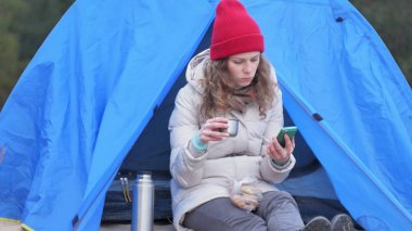 Kırmızı bir şapka çekici genç kadın turist turist çadırda oturur ve bir termos 4 k çay içer