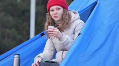 Kırmızı bir şapka çekici genç kadın turist turist çadırda oturur ve bir termos çay içer