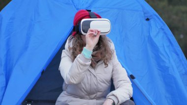 Kırmızı bir şapka çekici genç kadın turist turist çadırda oturur ve bir sanal gerçeklik kask sahiptir