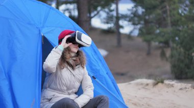 Kırmızı bir şapka çekici genç kadın turist turist çadırda oturur ve bir sanal gerçeklik kask sahiptir
