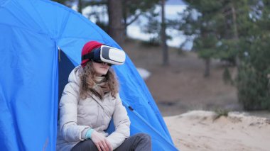Kırmızı bir şapka çekici genç kadın turist turist çadırda oturur ve bir sanal gerçeklik kask sahiptir