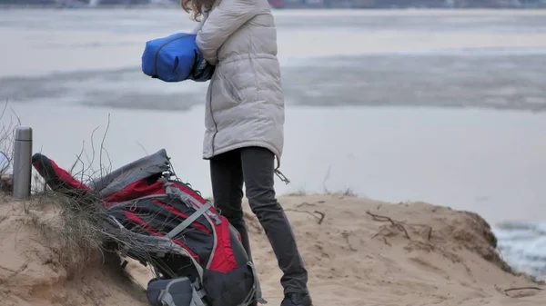 Attraente giovane donna turistica con un cappello rosso raccoglie una tenda turistica vicino alla foresta sulla costa — Foto Stock