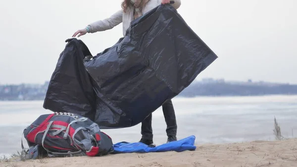 Attraente giovane donna turistica con un cappello rosso raccoglie una tenda turistica vicino alla foresta sulla costa — Foto Stock