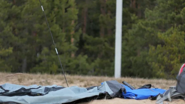 Attraente giovane donna turistica con un cappello rosso raccoglie una tenda turistica vicino alla foresta sulla costa — Foto Stock