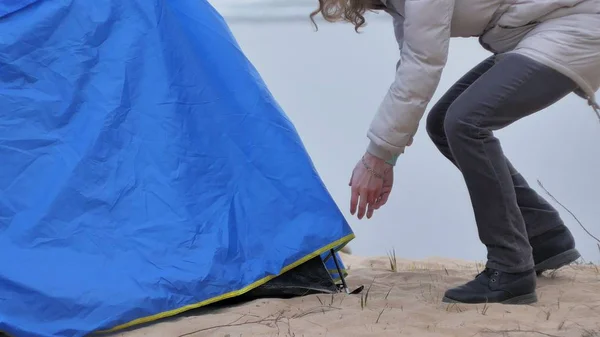 Attraente giovane donna turistica con un cappello rosso raccoglie una tenda turistica vicino alla foresta sulla costa — Foto Stock