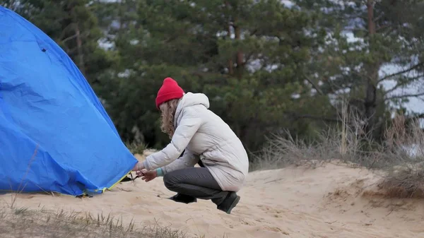 赤い帽子の魅力的な若い観光客女性が海岸の森の近くの観光テントを収集します。 — ストック写真