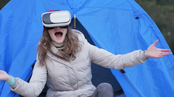 Atraente jovem turista em um chapéu vermelho senta-se em uma tenda turística e goza de um capacete realidade virtual — Fotografia de Stock