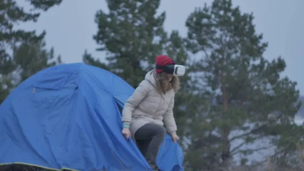 Привлекательная молодая туристка в красной шляпе сидит в туристической палатке и пользуется шлемом виртуальной реальности — стоковое фото