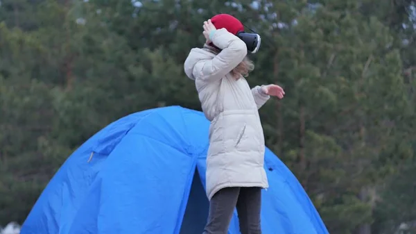 Attraente giovane donna turista con un cappello rosso si siede in una tenda turistica e gode di un casco realtà virtuale — Foto Stock