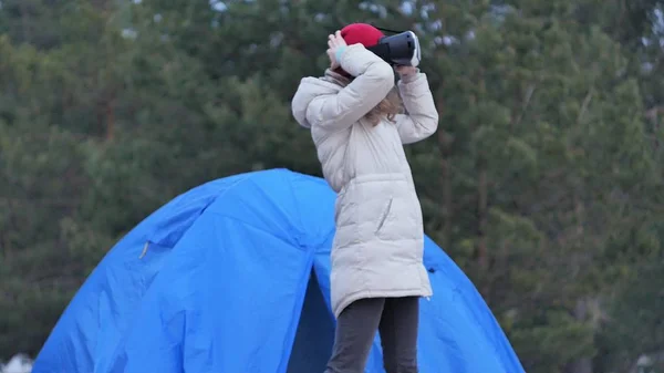Attraktiv ung kvinna turist i en röd hatt sitter i turist tält och åtnjuter en virtuell verklighet hjälm — Stockfoto