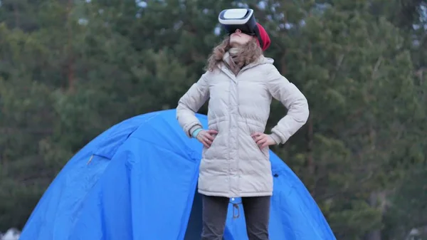 Atractiva joven turista con sombrero rojo se sienta en una carpa turística y disfruta de un casco de realidad virtual — Foto de Stock